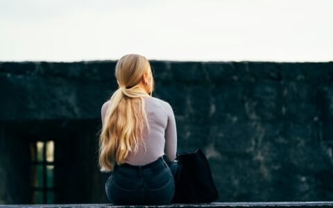 woman in white long sleeve shirt and black denim jeans sitting on gray concrete wall during